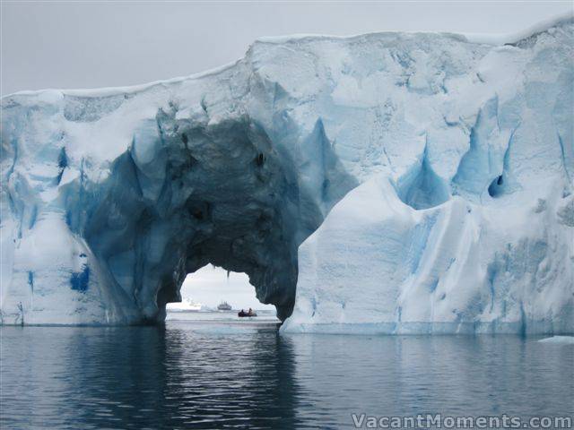 Clipper Adventurer in the far distance and a zodiac in the foreground through the iceberg tunnel